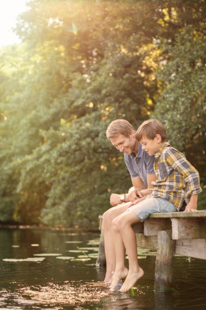 istock Father and son dangling feet in lake 555799499