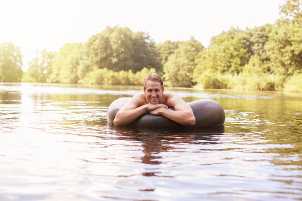 homem flutuando em tubo interno no lago - inner tube swimming lake water - fotografias e filmes do acervo