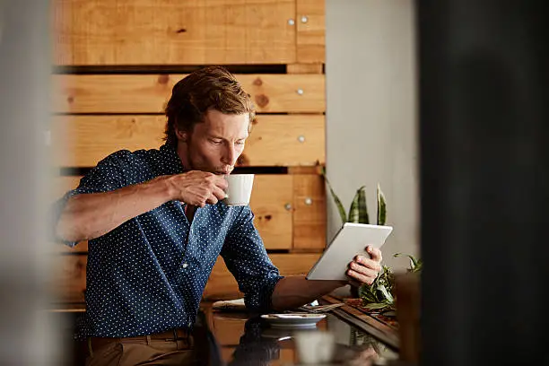 Photo of Man using tablet PC while having coffee at cafe