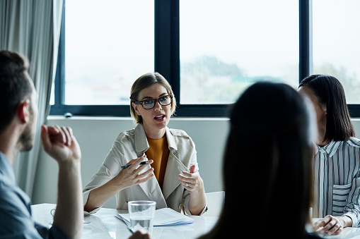 Young businesswoman discussing plan with colleagues at conference table