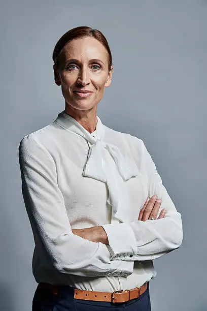 Portrait of confident mature businesswoman standing arms crossed over gray background