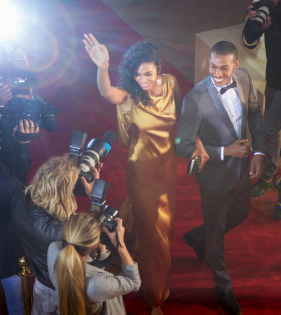 coppia di celebrità che salutano e vengono fotografati dai fotografi paparazzi all'evento sul tappeto rosso - evening gown flash foto e immagini stock