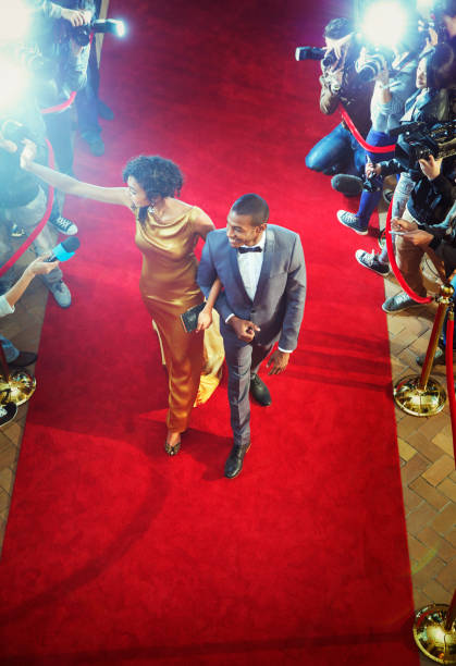 coppia di celebrità che arrivano all'evento salutando e camminando sul tappeto rosso - evening gown flash foto e immagini stock