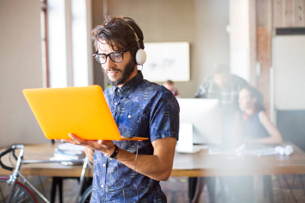 casual businessman wearing headphones and using laptop in office - day asian ethnicity asian culture asian and indian ethnicities imagens e fotografias de stock