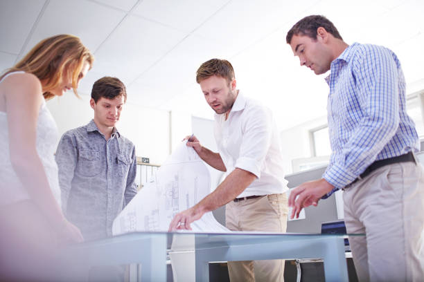 istock Architects reviewing blueprints in meeting in office 562873503