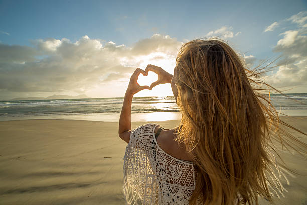 istock Woman on beach makes heart shape finger frame to sunset 564562828