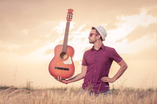 istock Young man holding guitar on the field 564563668
