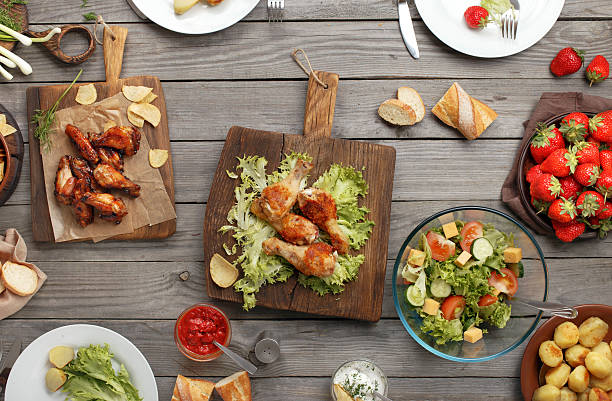 Different food cooked on the grill Outdoors Food Concept. On the wooden table different food, grilled chicken legs, buffalo wings, chips, bread, salad, potatoes and strawberry buffalo iowa stock pictures, royalty-free photos & images