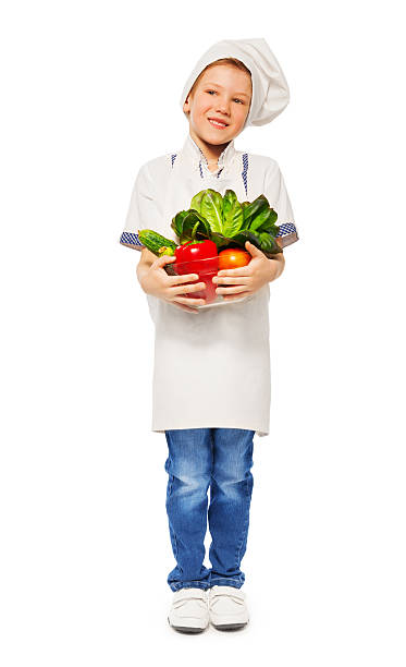 istock Boy in cook's uniform holding bowl with vegetables 564566940