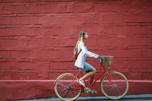 Young woman in blue dress rides a red vintage bike with basket in the streets of Moscow.