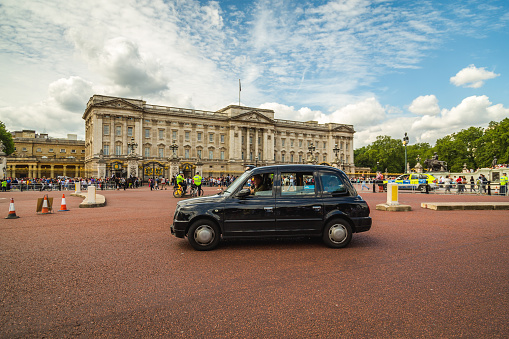 London, UK - June 28, 2016: A black taxi going past Buckingham Palace during the day. Large amounts of people can be seen.