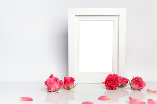 Blank photo frame, pink roses and petals on white table background