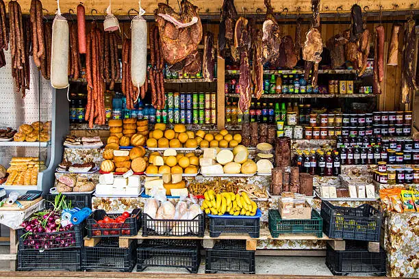 A colourful market stall at the top of the Transfagarasan road in Romania. The stall is packed with fresh produce, including cured meats and salami, fresh vegetables, pastries, soft drink and beer, and locally procudes wines and Tuica (plum liquor). Horizontal colour image with no people.