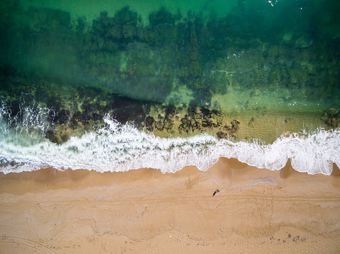 Aerial view of man standing at coastline. Sea, waves, algae and sand.Beach detail