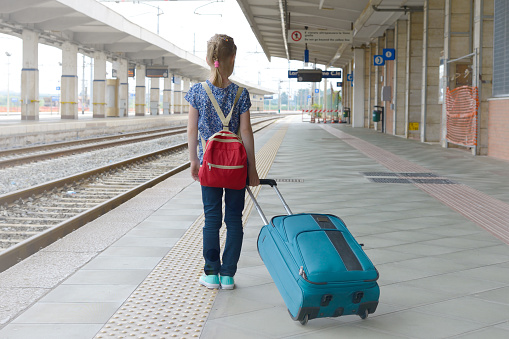 child with a suitcase on an empty train station