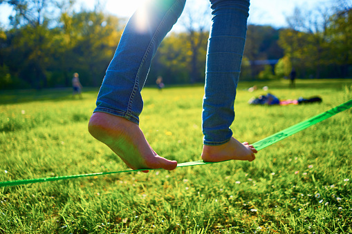 Photo of a young woman walking/ balancing on a slackline rope in the evening light.