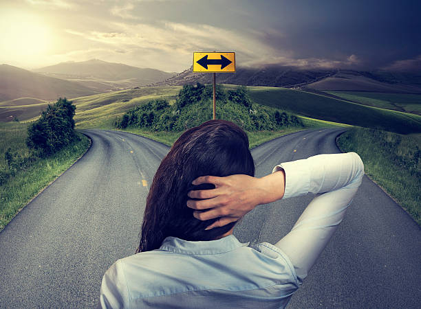business woman in front of two roads thinking deciding business woman in front of two roads thinking deciding hoping for best taking chance crossroads sign stock pictures, royalty-free photos & images