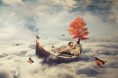 Young lonely woman drifting on boat above clouds. Dreamy screensaver