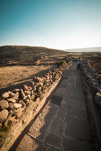 Tourist walking on the Inca Trail at sunset, Amantani' Island, Titicaca Lake, among the most scenic travel destination in Peru. Travel adventures and vacations in the Americas. Toned image, vintage style.