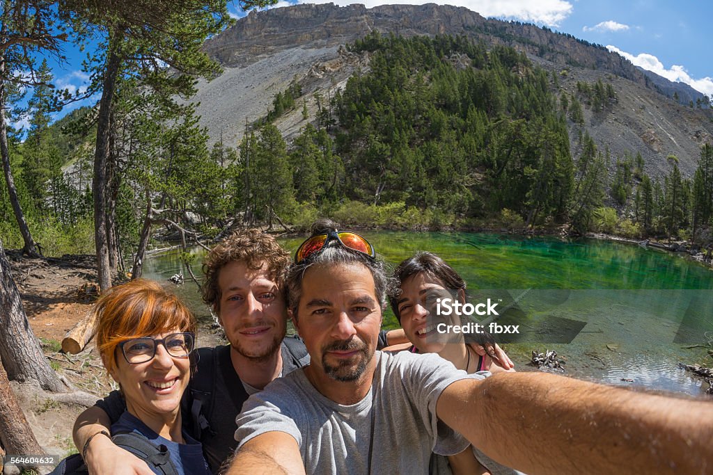 Selfie in scenic high altitude landscape on the Alps Four young people taking selfie in idyllic landscape with green lake, conifer woodland and mountains in background. Scenic fisheye distortion. Concept of traveling people and nature beauty exploration. Green Color Stock Photo