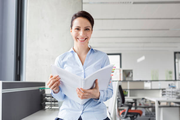 istock Portrait smiling businesswoman holding report in office 567166317