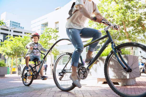 filho de capacete andando de bicicleta com a mãe em parque urbano - cycling bicycle healthy lifestyle green - fotografias e filmes do acervo