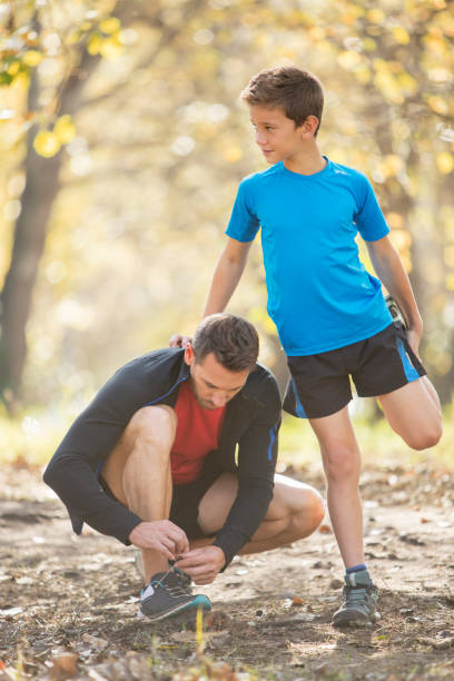 Boy balances across wooden stumps outdoors with guidance from a trainer. The activity promotes coordination, agility, and balance as part of outdoor sports exercises for children.