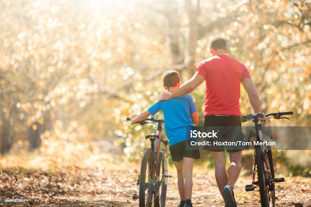 Affectionate father and son walking mountain bikes on path in woods  Cycling Stock Photo
