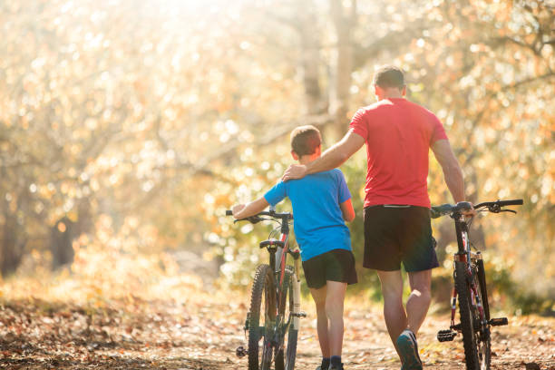 Affectionate father and son walking mountain bikes on path in woods  mountain biking stock pictures, royalty-free photos & images