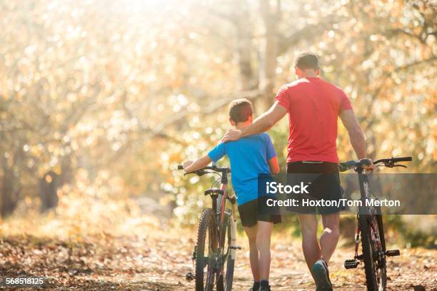 Affectionate Father And Son Walking Mountain Bikes On Path In Woods Stock Photo - Download Image Now