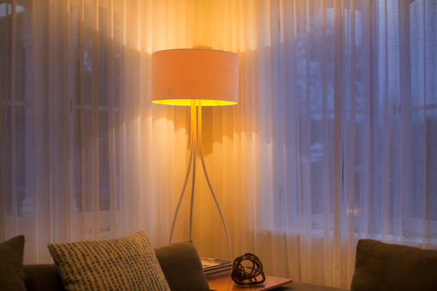 istock Illuminated floor lamp at window with sheer curtains 568518587