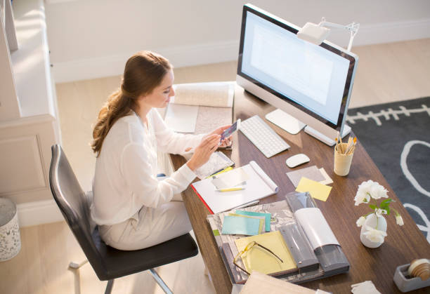 istock Interior designer texting on cell phone at desk in home office 568518611