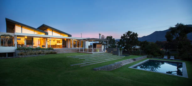 istock Illuminated modern house beyond yard and swimming pool at night 568518905