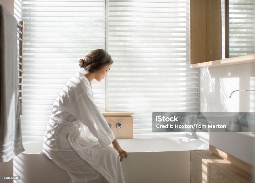 Woman in bathrobe drawing a bath in soaking tub in luxury bathroom  20-24 Years Stock Photo