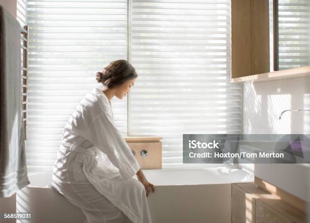 Woman In Bathrobe Drawing A Bath In Soaking Tub In Luxury Bathroom Stock Photo - Download Image Now