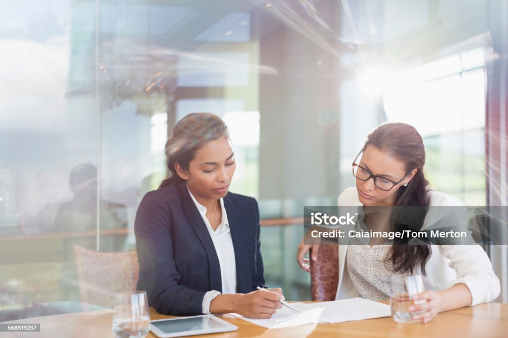 Businesswomen reviewing paperwork in conference room  25-29 Years Stock Photo