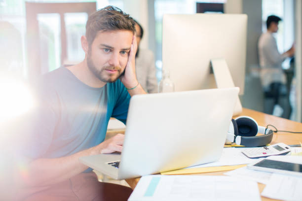 istock Serious creative businessman using laptop with head in hands in office 568519369