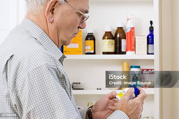 Man Reading Label On Bottle Of Tablets Stock Photo - Download Image Now - Medicine Cabinet, Senior Adult, Aspirin