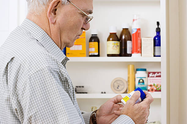 homem lendo label em frasco de comprimidos - medicine cabinet fotos - fotografias e filmes do acervo