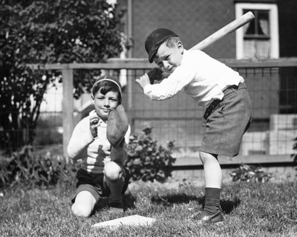 Two boys (6-7) playing baseball in garden, (B&W)  baseball sport photos stock pictures, royalty-free photos & images