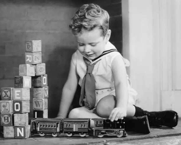 Photo of Boy (4-5) playing with model train set on floor, (B&W),