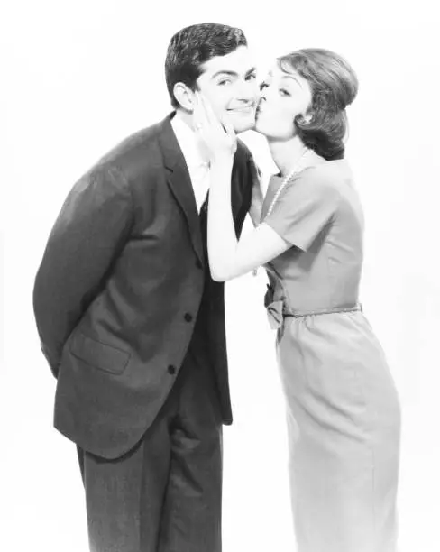 Photo of Woman kissing man on cheek in studio, (B&W)