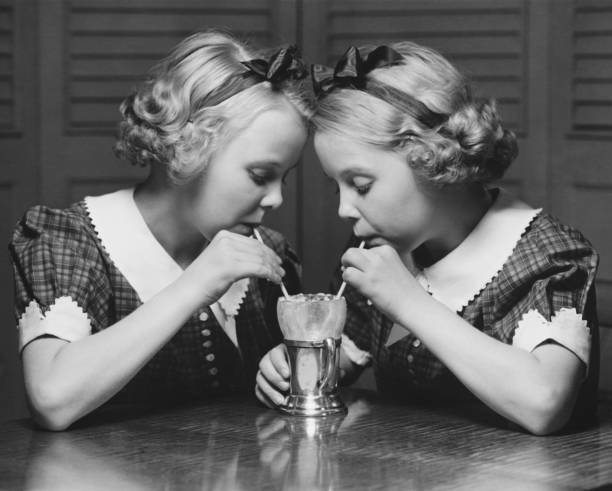 Twin sisters (12-13) drinking through straws from same glass, (B&W)  milkshake photos stock pictures, royalty-free photos & images