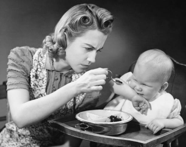 Mother trying to feed unwilling baby (9-12 months), (B&W)  spoon photos stock pictures, royalty-free photos & images