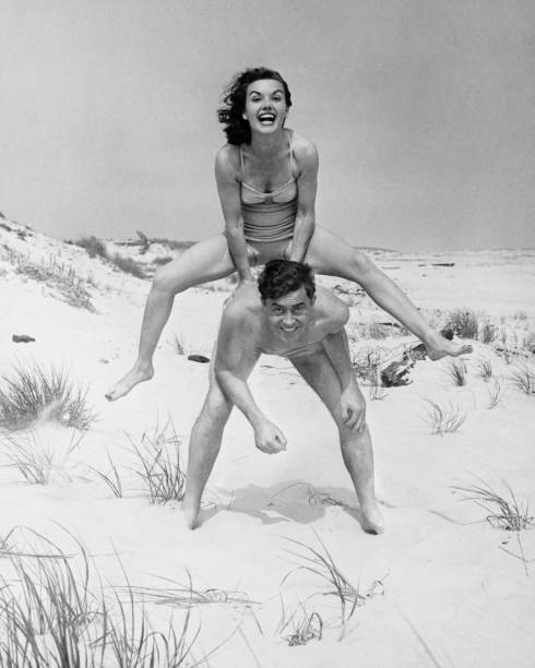 Young couple on beach, woman leap-frogging man, (B&W), portrait  black and white beach stock pictures, royalty-free photos & images