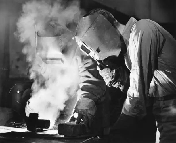Photo of Two men welding, holding protective masks, (B&W)