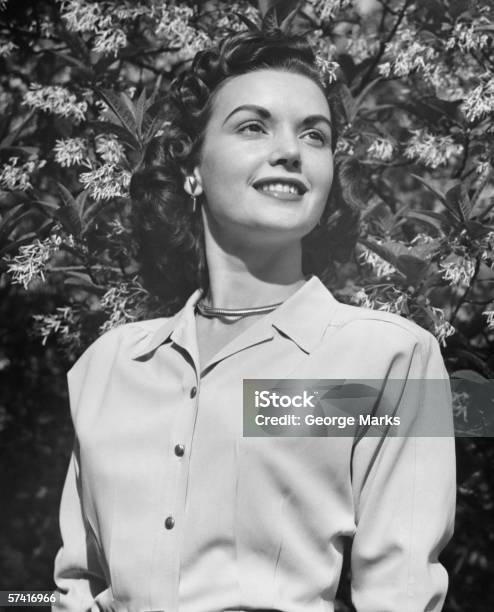 Joven Mujer Posando Por Árbol De Flor Abriéndose Foto de stock y más banco de imágenes de Mujeres - Mujeres, 1940-1949, Una sola mujer