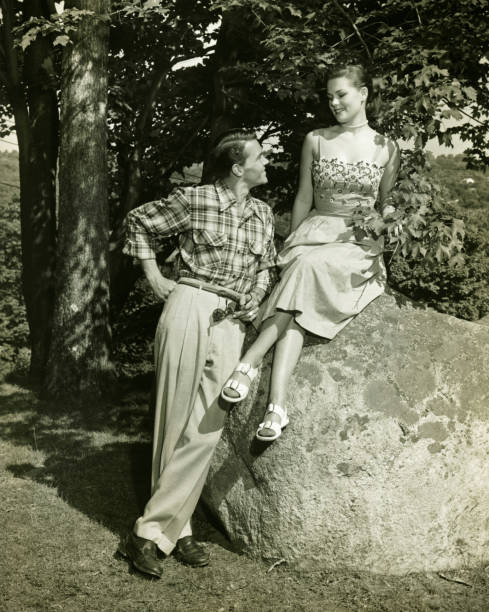 giovane coppia in posa nel parco, (b & w - 1950s style couple old fashioned heterosexual couple foto e immagini stock