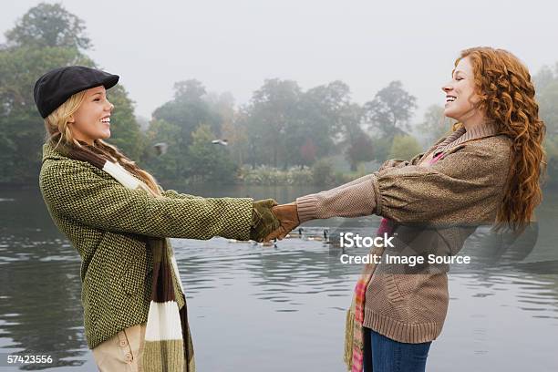 Two Young Women Holding Hands In Park Stock Photo - Download Image Now - Cap - Hat, England, Retro Style