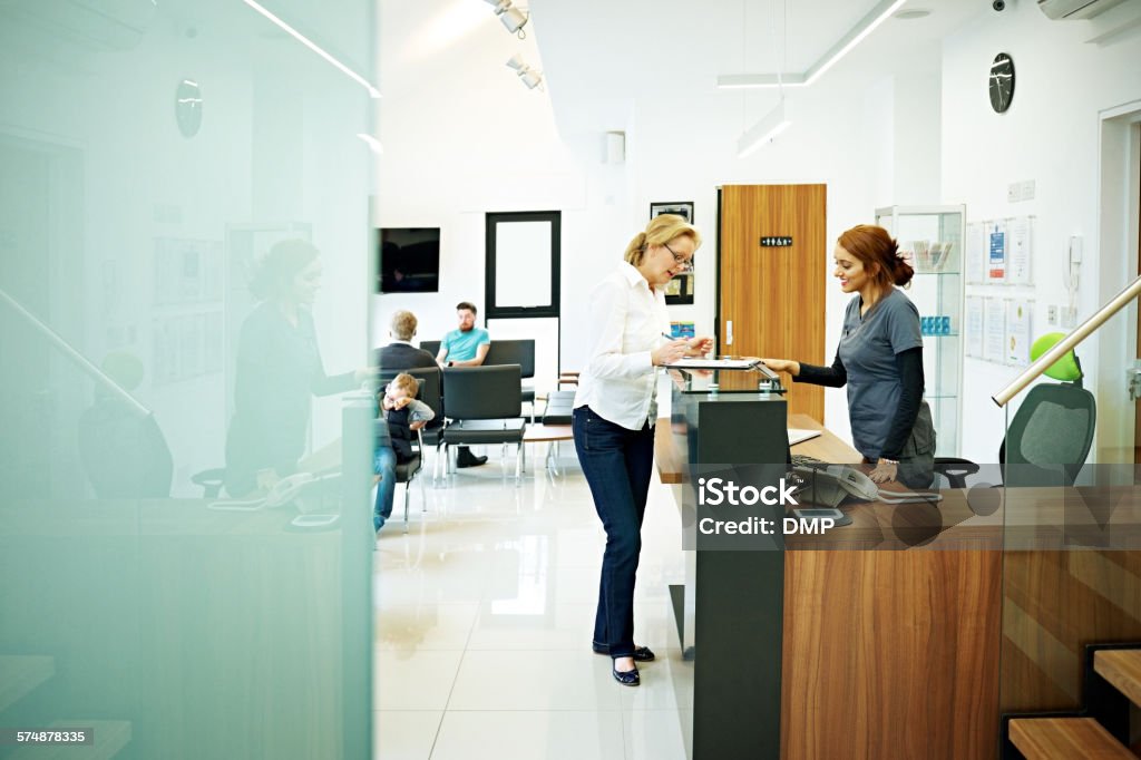 Mature female patient at dental clinic Mature woman standing at the reception desk in a dental clinic filling out the papers Receptionist Stock Photo